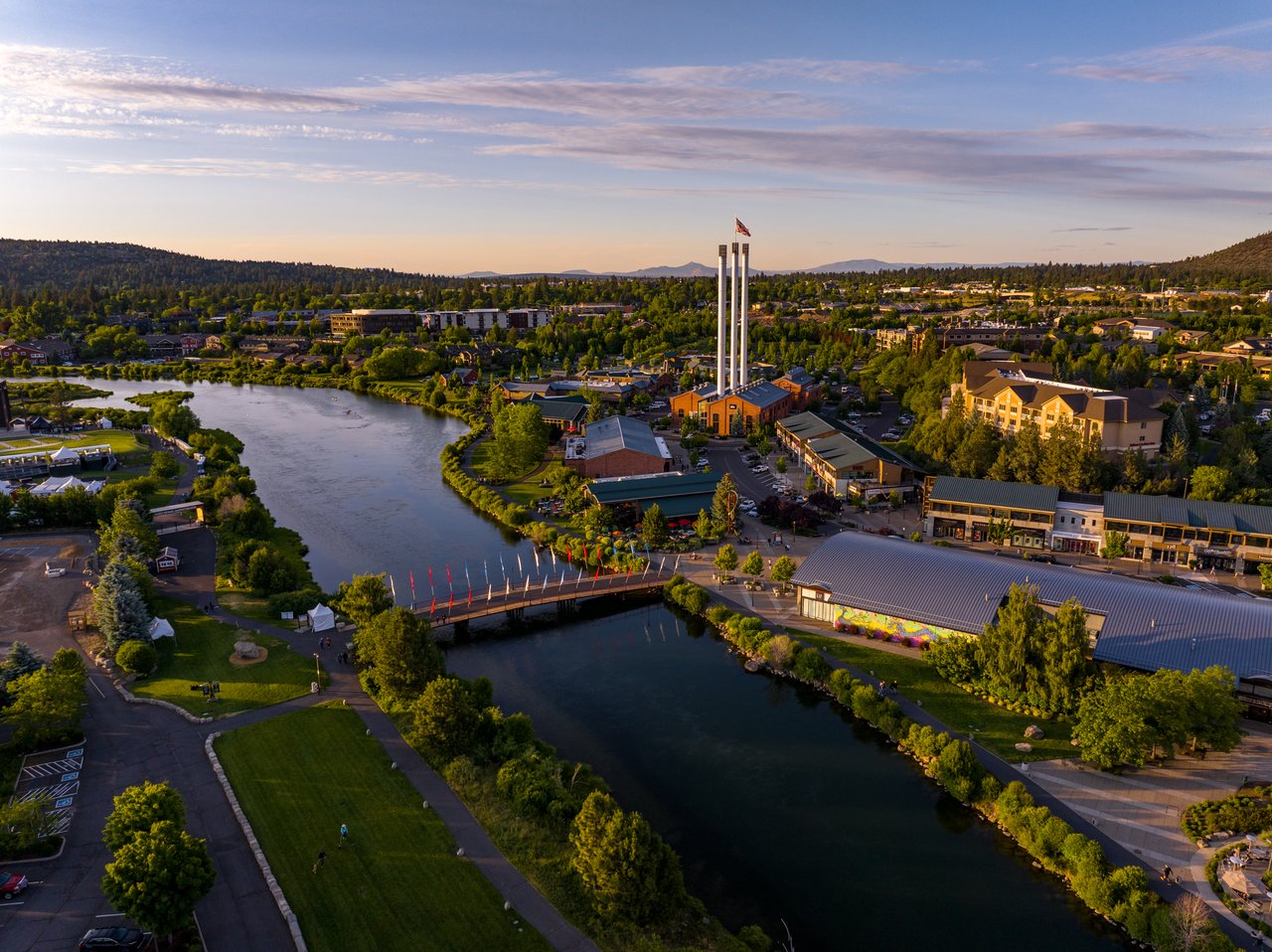 Warm sunset aerial of Bend’s Old Mill District with the Deschutes River curving through the foreground
